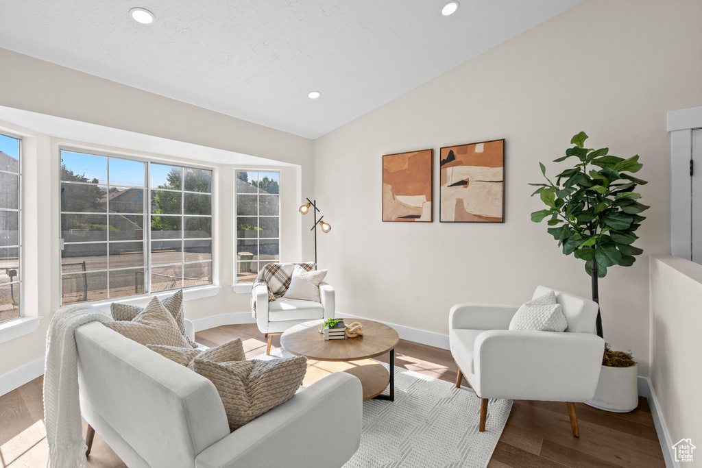 Living area featuring plenty of natural light, lofted ceiling, recessed lighting, wood finished floors, and baseboards