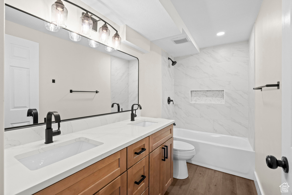 Bathroom featuring double vanity, wood finished floors, toilet, tub / shower combination, and recessed lighting