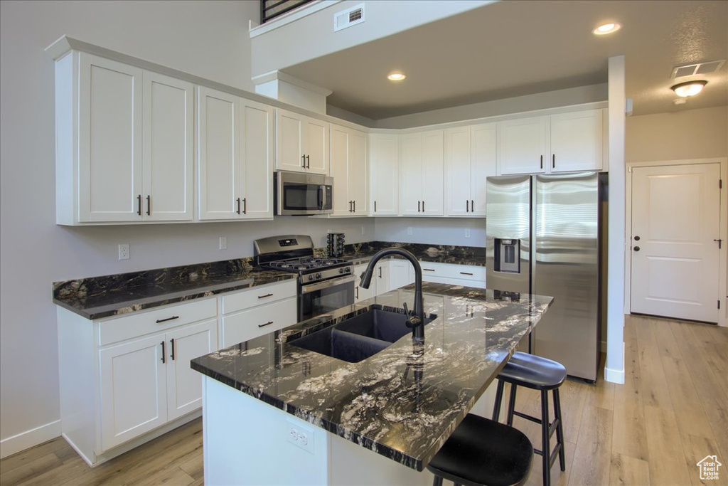 Kitchen featuring stainless steel appliances, a sink, light wood-style floors, white cabinets, and dark stone countertops