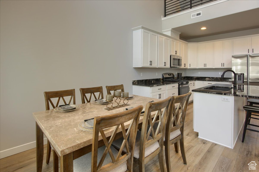 Kitchen with stainless steel appliances, a sink, white cabinets, light wood-style floors, and a high ceiling