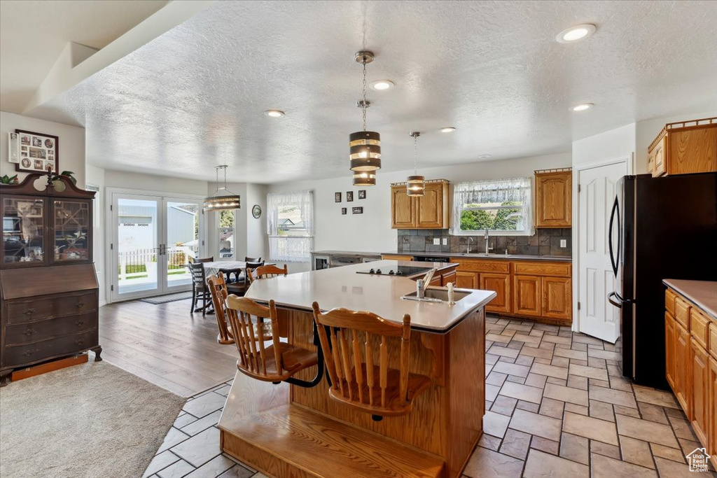 Kitchen featuring freestanding refrigerator, an island with sink, a textured ceiling, decorative backsplash, and a sink