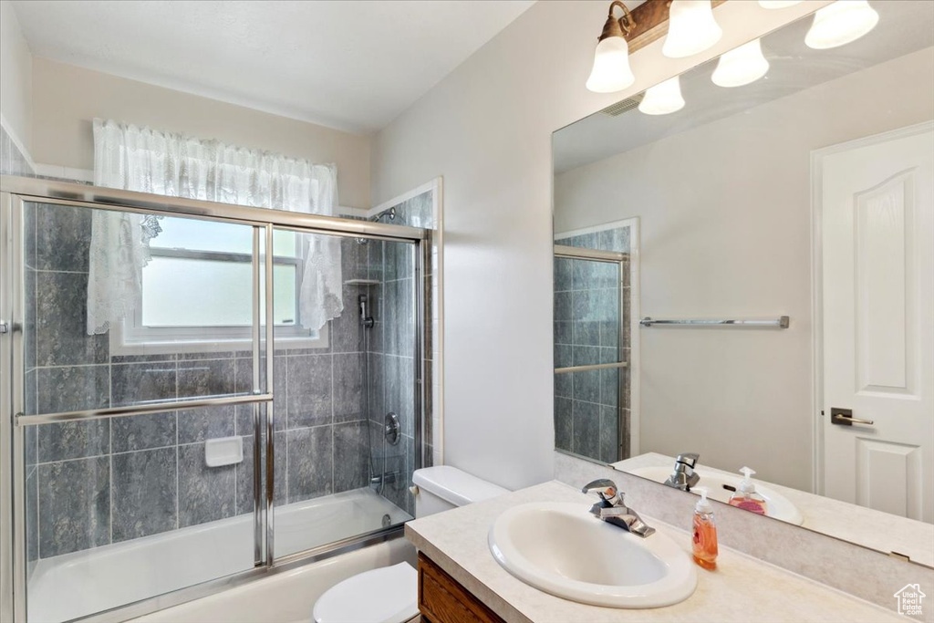 Bathroom with toilet, vanity, and bath / shower combo with glass door
