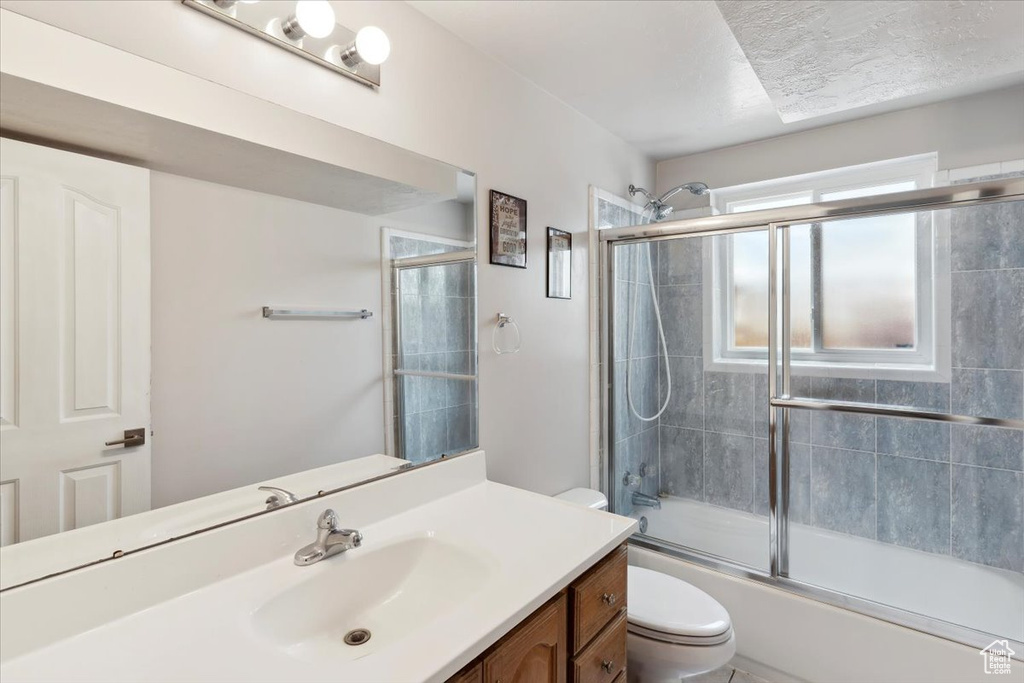Bathroom with toilet, vanity, and bath / shower combo with glass door