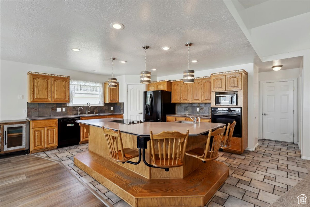 Kitchen with black appliances, an island with sink, a textured ceiling, tasteful backsplash, and a sink