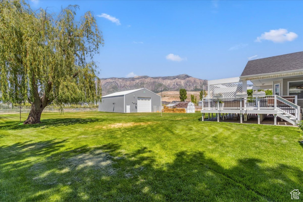 View of grassy yard with a detached garage, an outbuilding, a deck with mountain view, and stairs