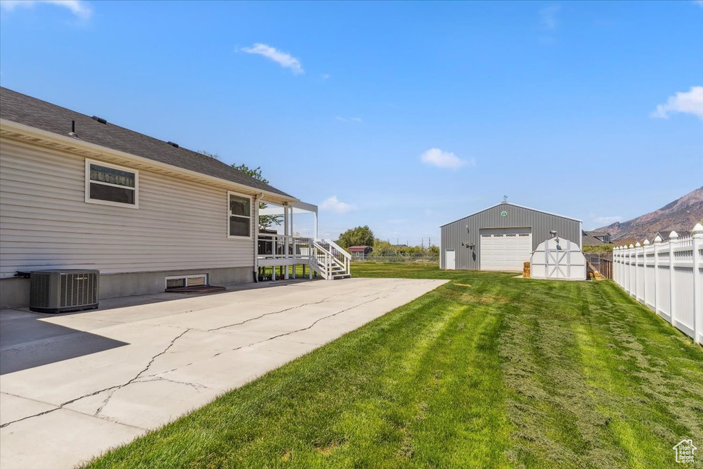 View of yard with central AC, a detached garage, an outbuilding, and driveway