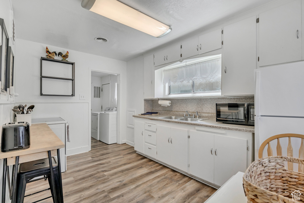Kitchen with black microwave, freestanding refrigerator, a sink, washer and dryer, and light countertops