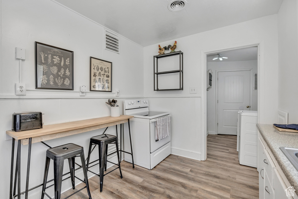 Kitchen featuring white range with electric cooktop, light wood-type flooring, a breakfast bar area, and a sink