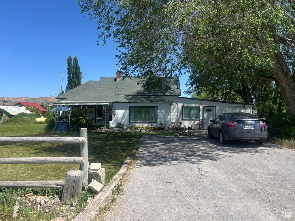 View of front of house featuring a front yard, a chimney, asphalt driveway, and a shingled roof