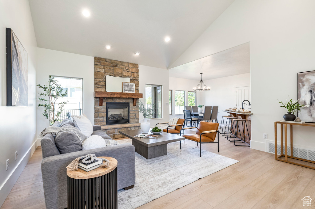 Living area featuring a stone fireplace, light wood-style floors, baseboards, recessed lighting, and a chandelier