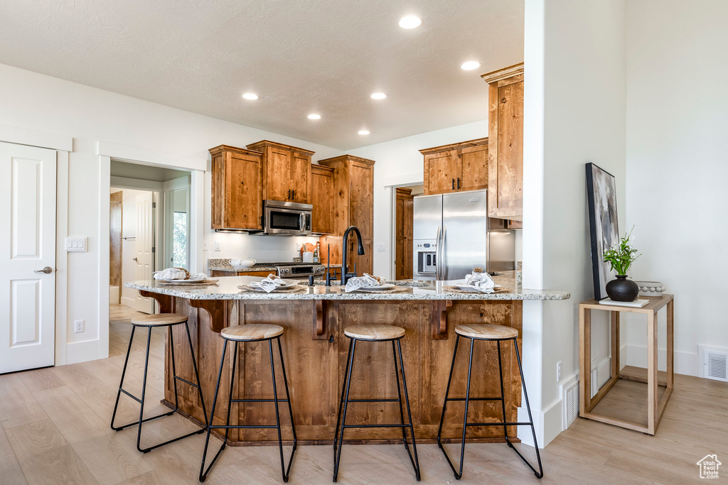 Kitchen with appliances with stainless steel finishes, light wood-style floors, a peninsula, light stone counters, and recessed lighting