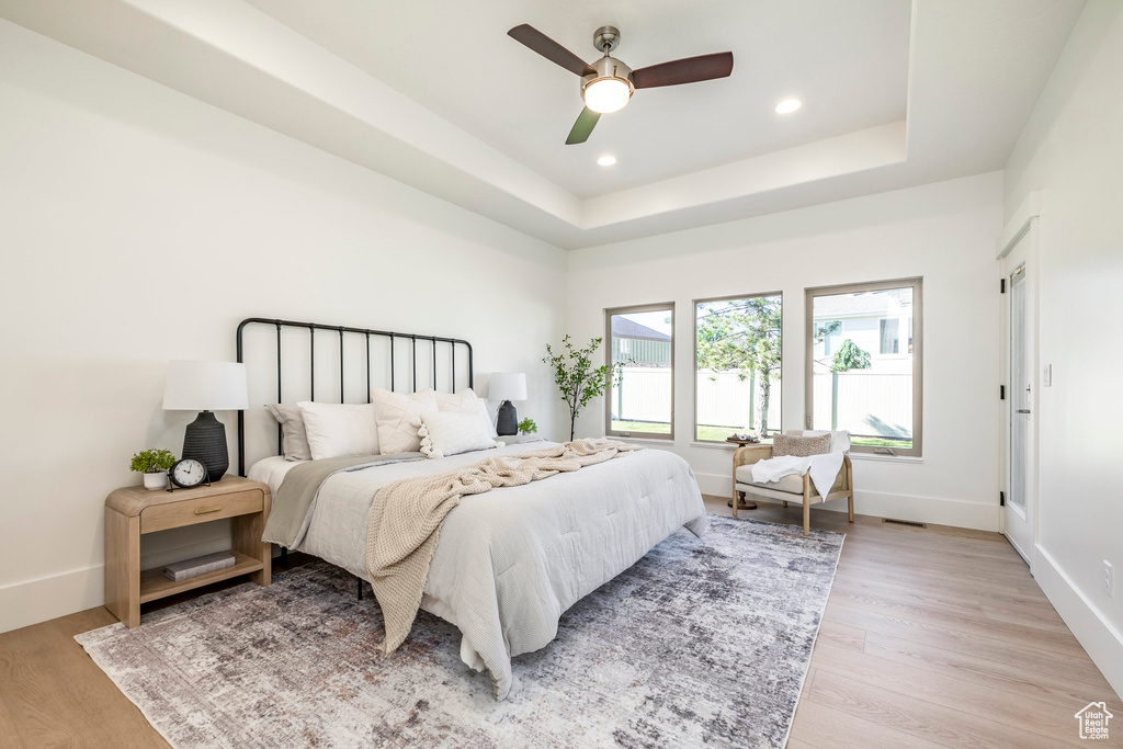 Bedroom featuring light wood-type flooring, baseboards, recessed lighting, a tray ceiling, and ceiling fan