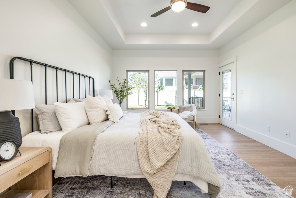 Bedroom featuring wood finished floors, a raised ceiling, baseboards, recessed lighting, and access to exterior