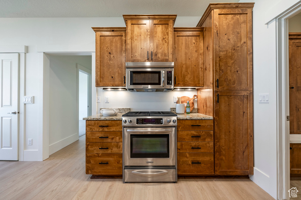Kitchen with stainless steel appliances, brown cabinets, and light wood-style floors