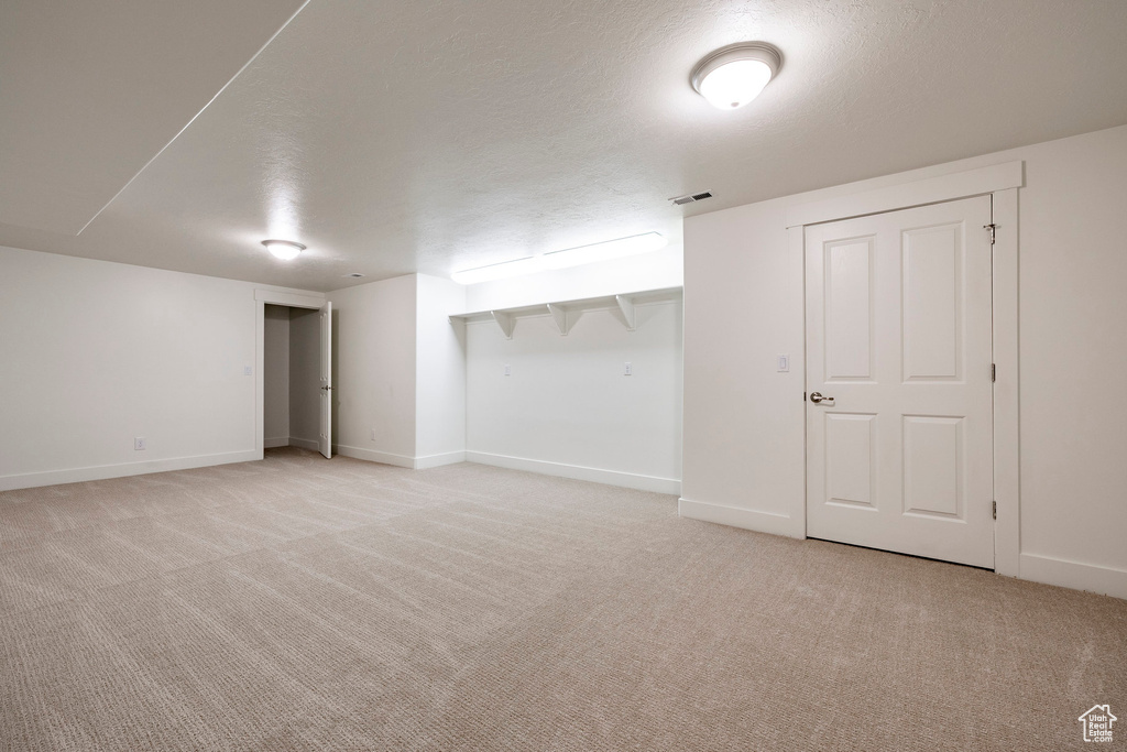 Finished basement featuring light carpet, baseboards, and a textured ceiling