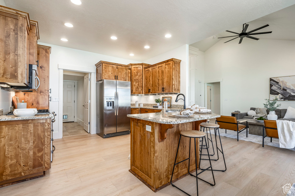 Kitchen featuring stainless steel fridge with ice dispenser, a peninsula, light wood-type flooring, open floor plan, and vaulted ceiling