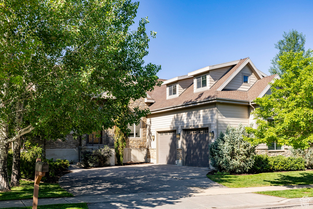 View of front facade with stone siding, concrete driveway, and a shingled roof