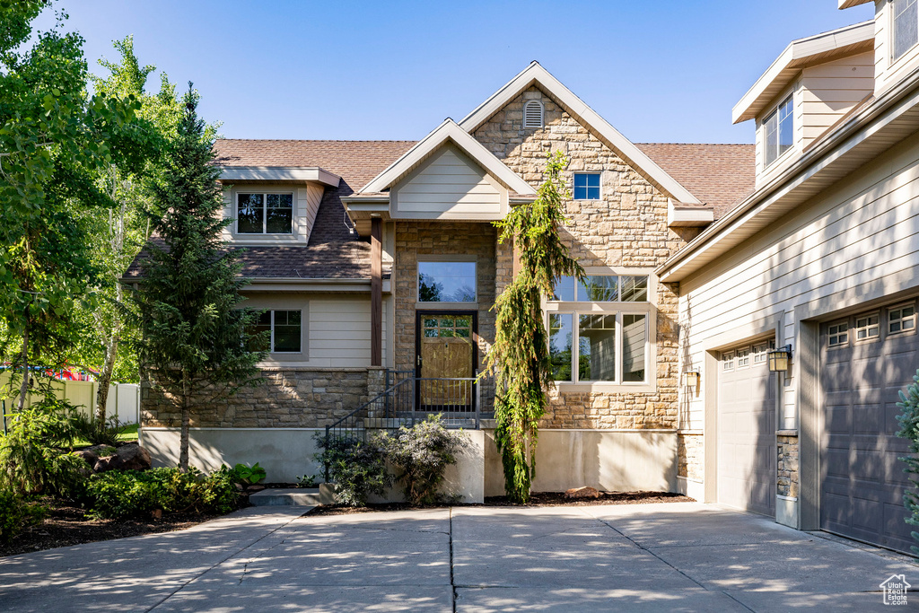 View of front of house featuring stone siding, concrete driveway, roof with shingles, and a garage
