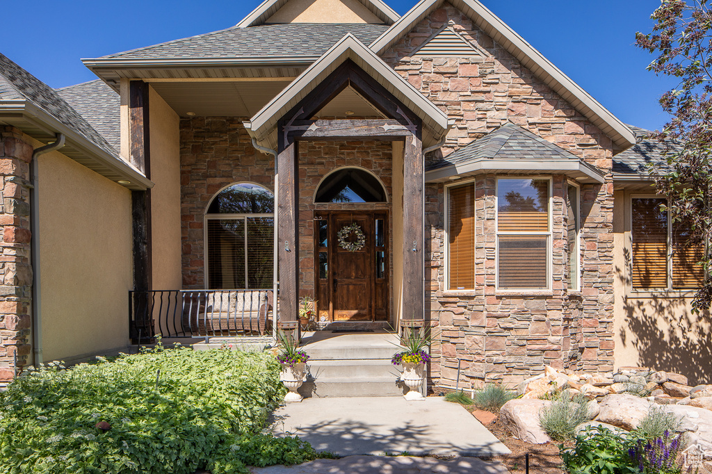 View of exterior entry featuring stone siding, stucco siding, and a shingled roof