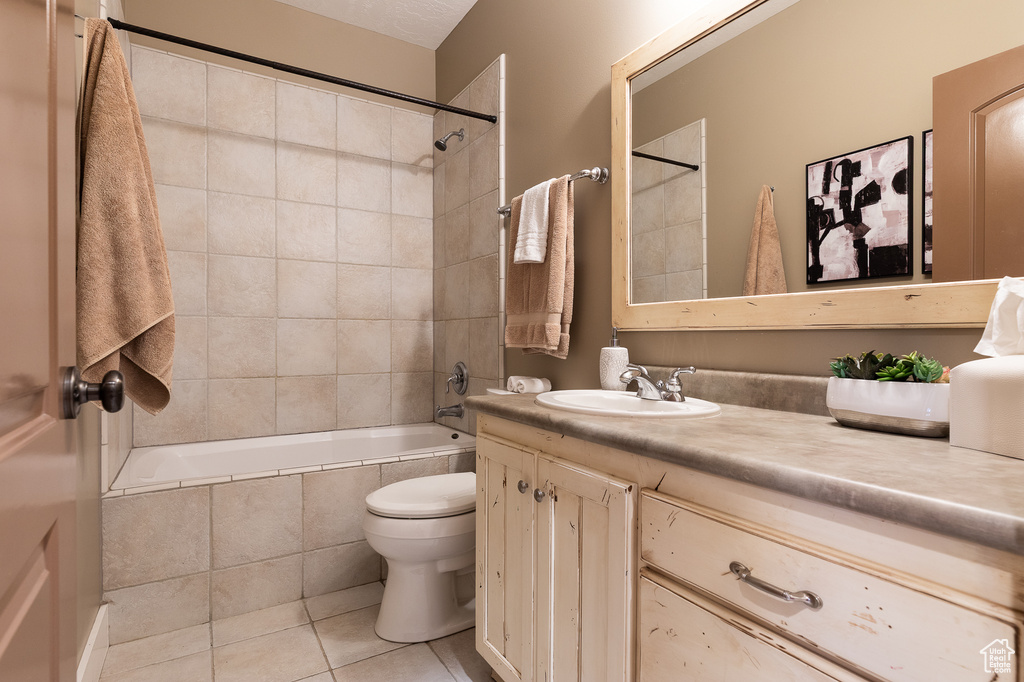 Full bath with tile patterned floors, toilet, vanity, and tiled shower / bath combo