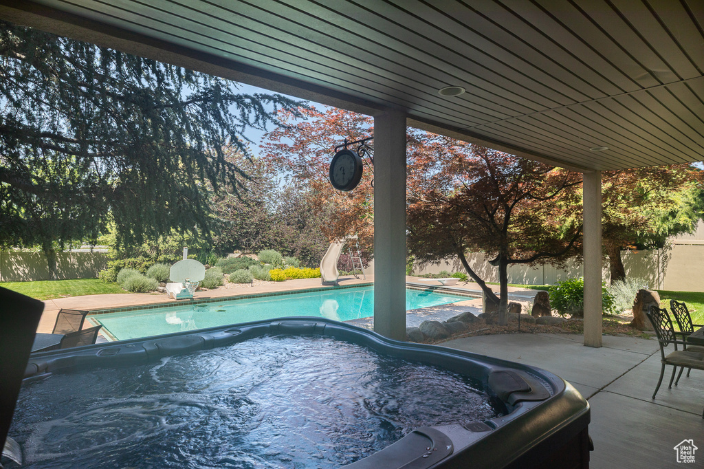 View of pool with a hot tub, a water slide, and a patio