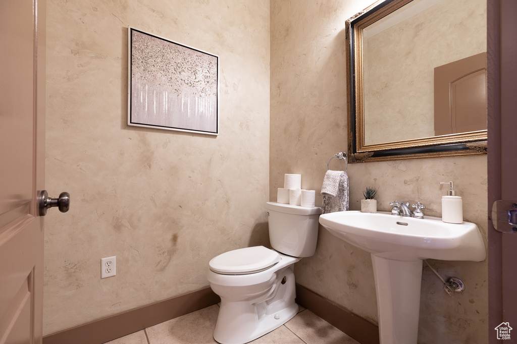 Half bathroom with toilet, tile patterned floors, a sink, and baseboards