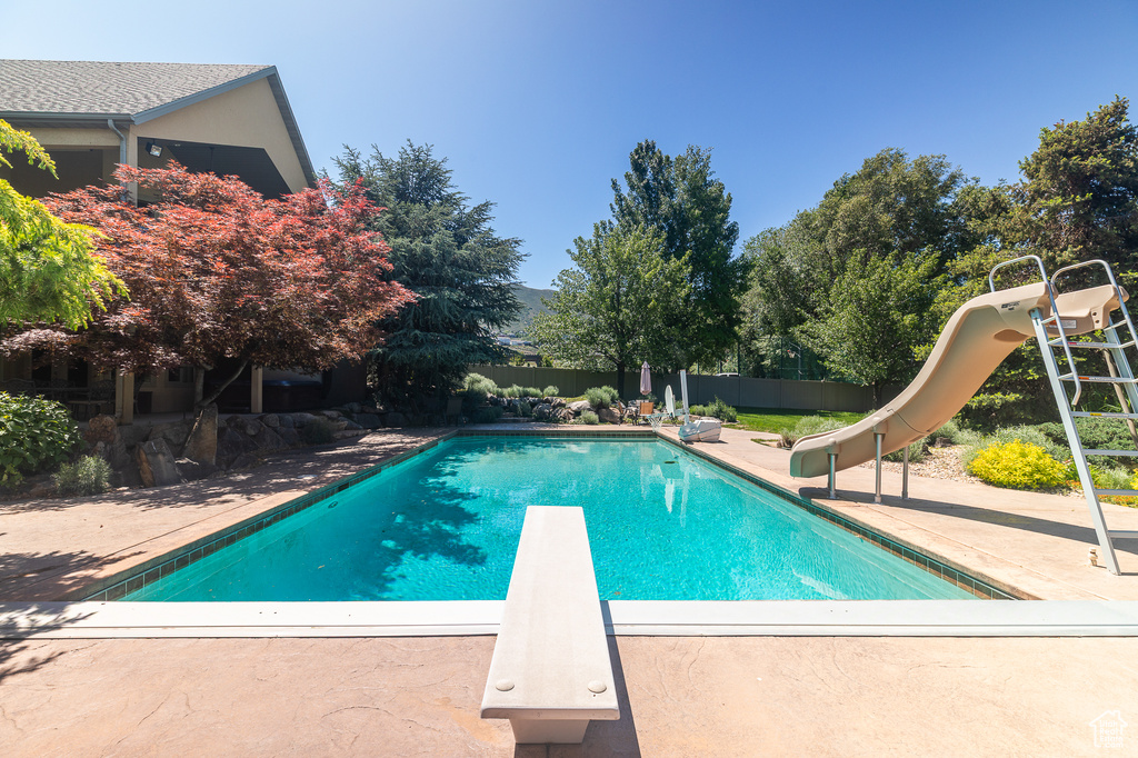 View of swimming pool with a water slide, a diving board, and a patio