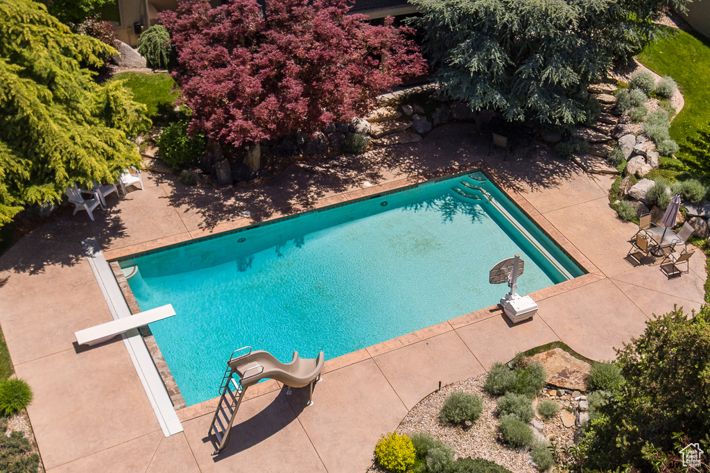 Outdoor pool with a water slide, a diving board, and a patio