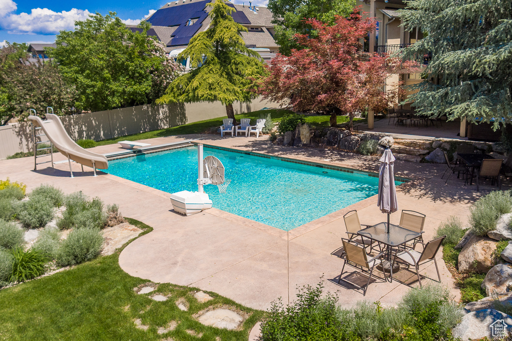 View of swimming pool with a patio area, a water slide, and a diving board