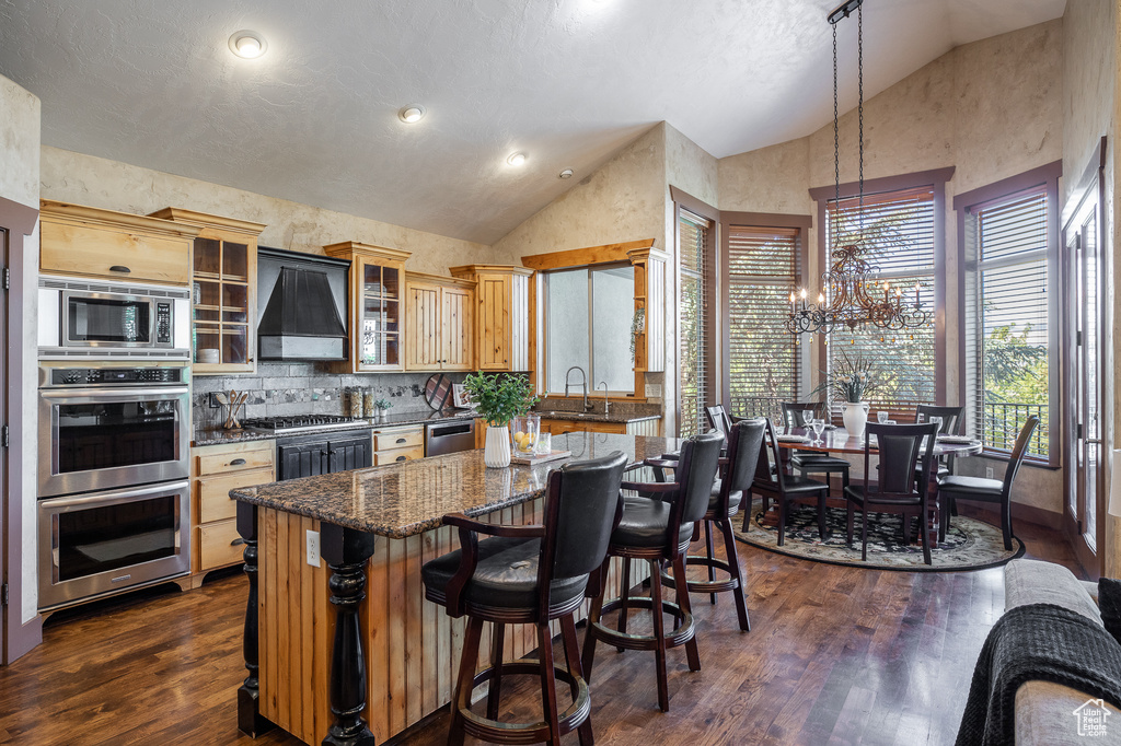 Kitchen featuring custom range hood, high vaulted ceiling, stainless steel appliances, a chandelier, and a center island