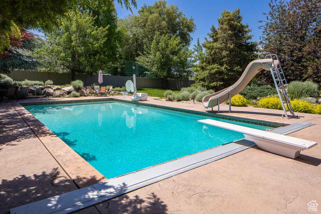 View of swimming pool featuring a water slide, a diving board, a fenced backyard, and a patio