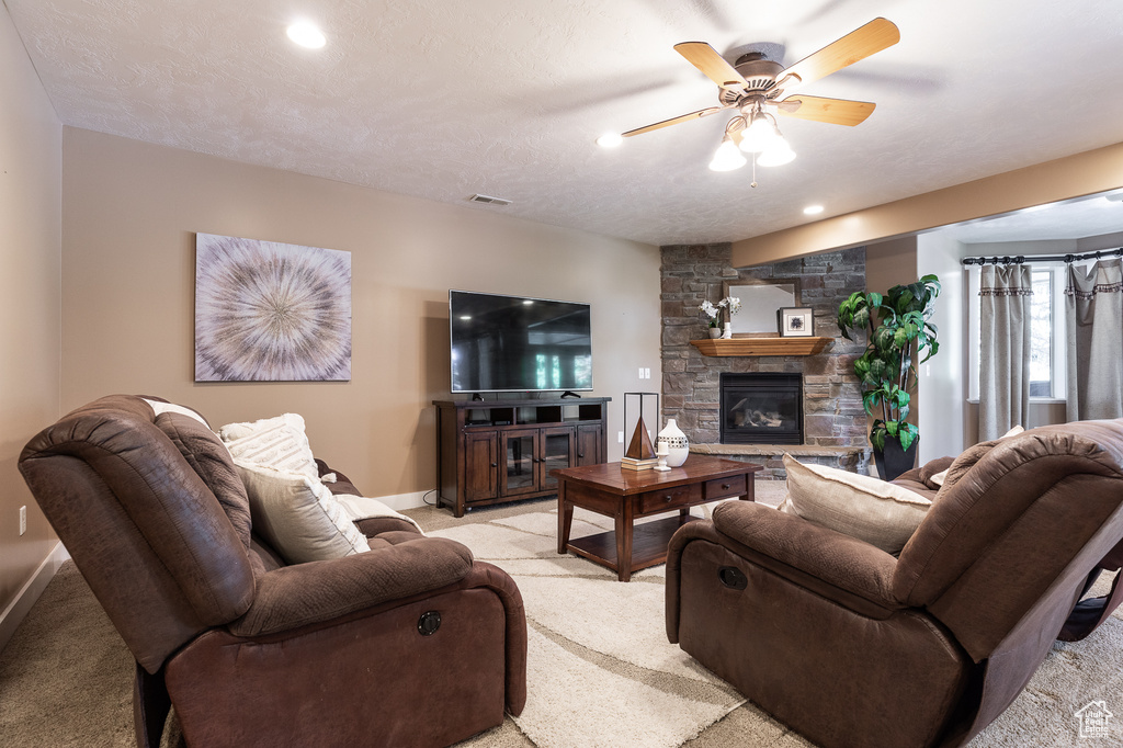 Living room with light carpet, a ceiling fan, baseboards, a stone fireplace, and recessed lighting