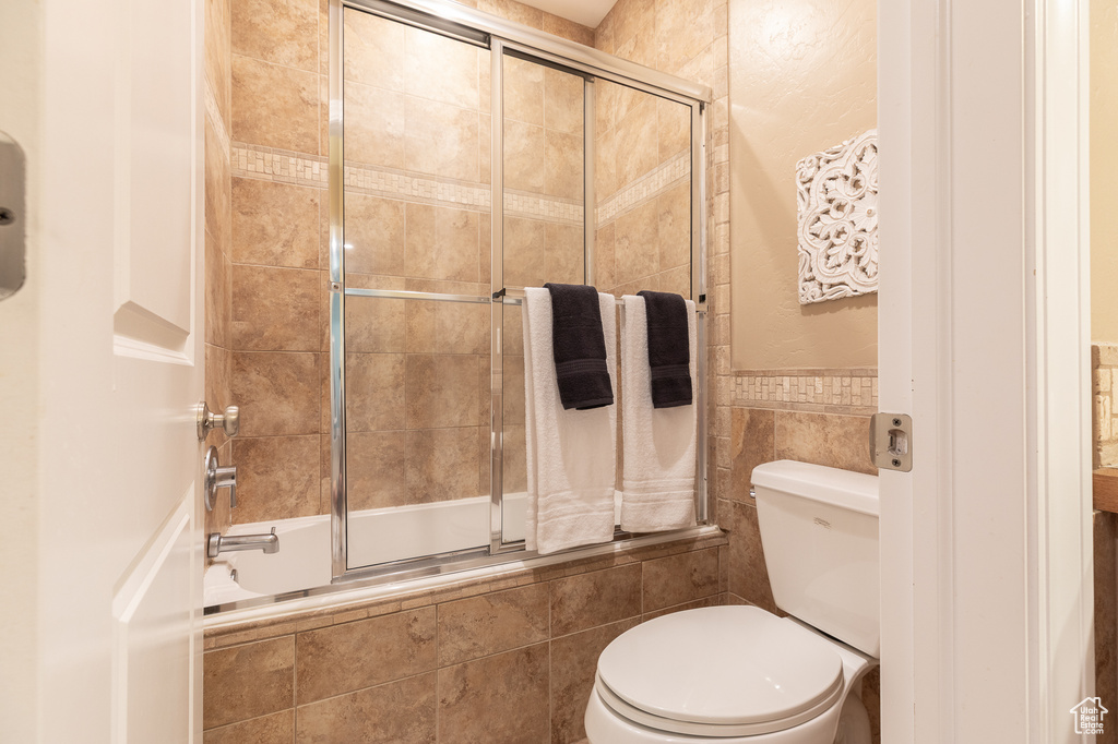 Bathroom with tiled shower / bath, toilet, tile walls, and wainscoting