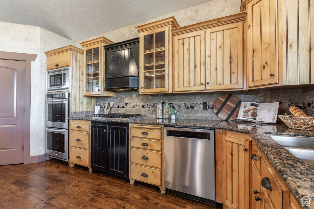 Kitchen featuring stainless steel appliances, dark wood finished floors, backsplash, and custom exhaust hood