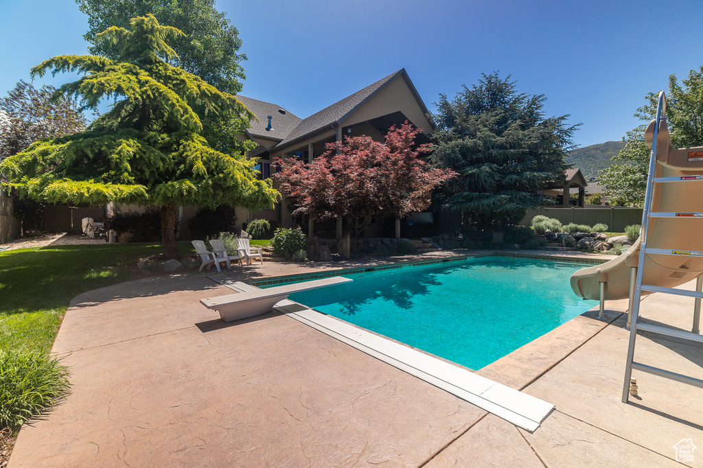View of swimming pool with a water slide, a patio area, a fenced backyard, and a diving board