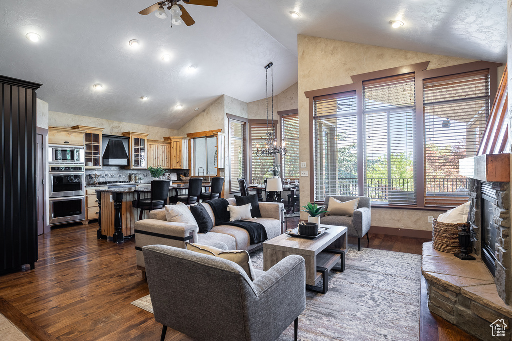 Living area with dark wood-type flooring, high vaulted ceiling, healthy amount of natural light, a ceiling fan, and a chandelier