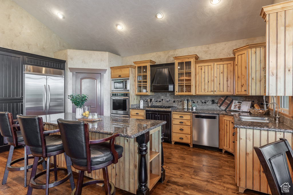 Kitchen featuring built in appliances, custom range hood, a sink, a center island, and dark wood finished floors