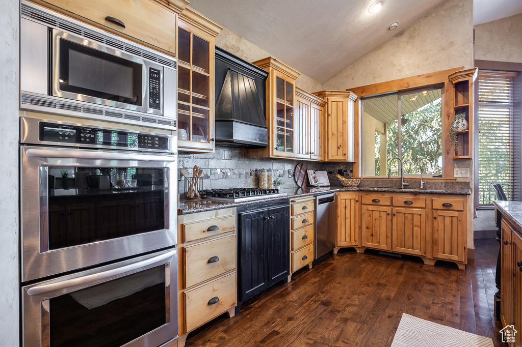 Kitchen featuring appliances with stainless steel finishes, a sink, vaulted ceiling, dark wood finished floors, and custom exhaust hood