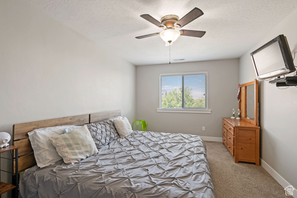 Bedroom with light colored carpet, a textured ceiling, baseboards, and ceiling fan