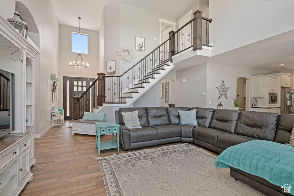 Living area with a high ceiling, light wood finished floors, arched walkways, a chandelier, and stairs