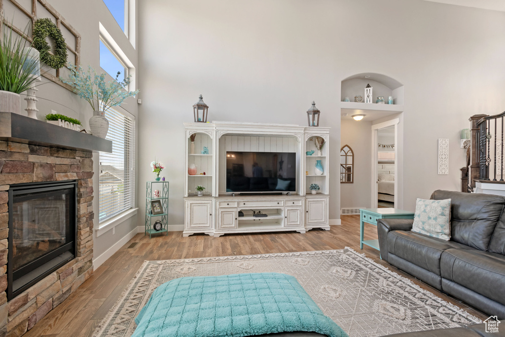 Living area featuring a high ceiling, light wood-style floors, a stone fireplace, and baseboards