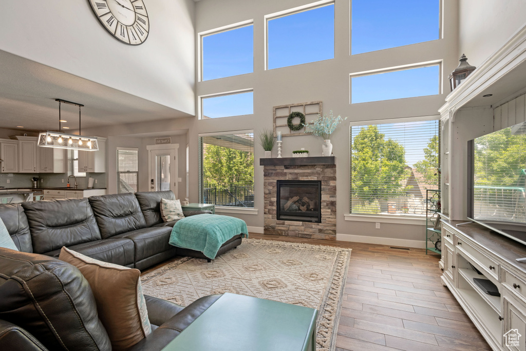 Living area featuring plenty of natural light, light wood finished floors, a towering ceiling, and a stone fireplace