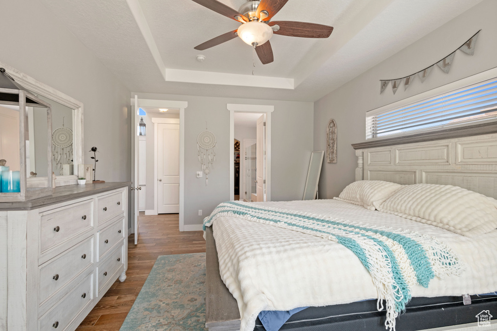Bedroom with a raised ceiling, dark wood-style floors, baseboards, and ceiling fan