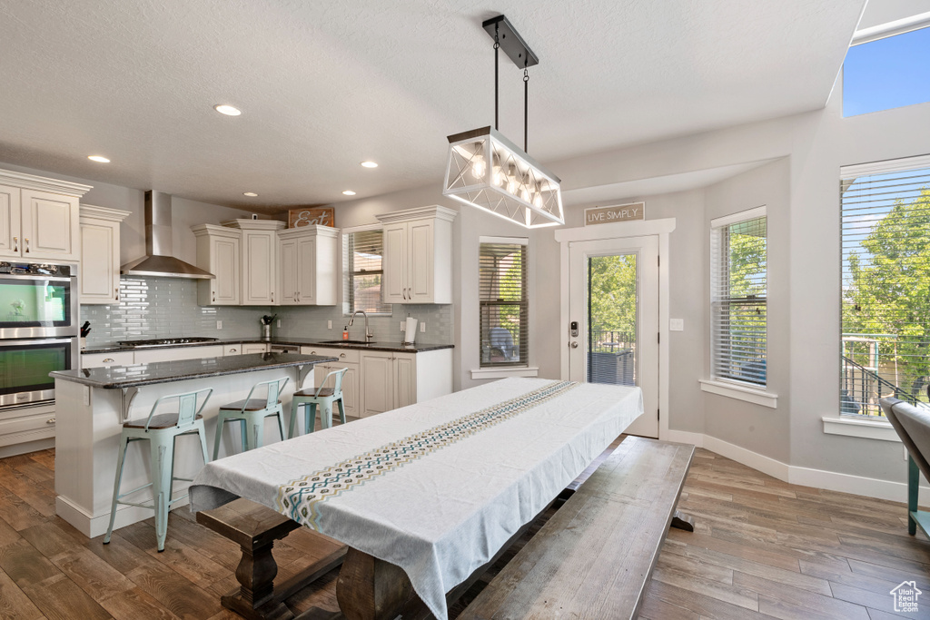 Kitchen featuring wall chimney range hood, stainless steel double oven, backsplash, black cooktop, and wood finished floors