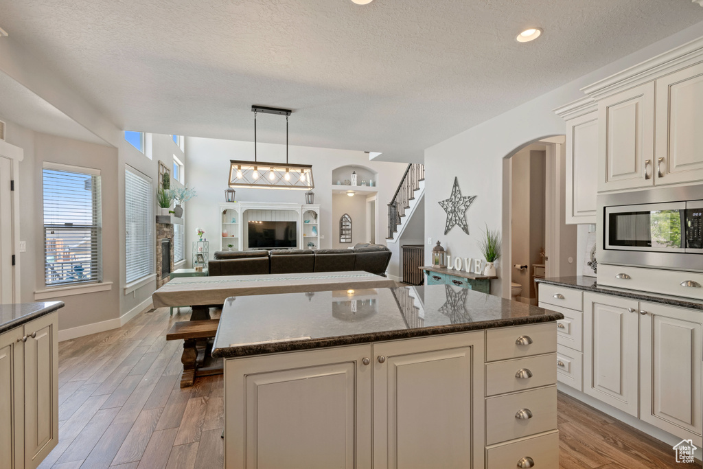 Kitchen featuring stainless steel microwave, arched walkways, light wood-type flooring, open floor plan, and a textured ceiling