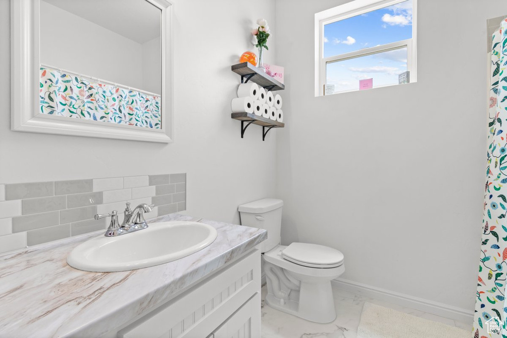 Bathroom featuring decorative backsplash, vanity, toilet, marble finish flooring, and baseboards