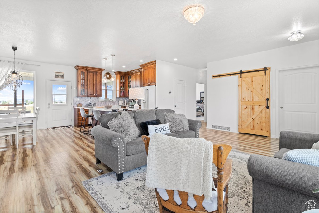 Living room featuring light wood-type flooring, a barn door, recessed lighting, and a chandelier