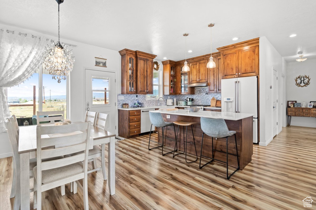 Kitchen with high end white refrigerator, stainless steel dishwasher, brown cabinetry, light wood-style floors, and backsplash