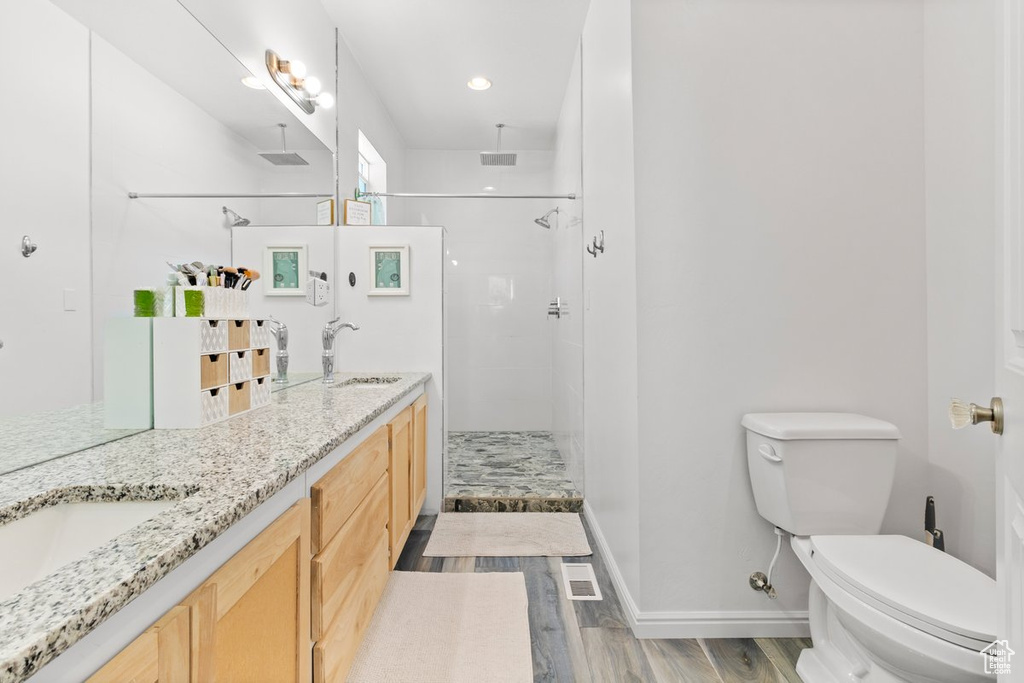 Bathroom featuring wood finished floors, toilet, a stall shower, double vanity, and baseboards
