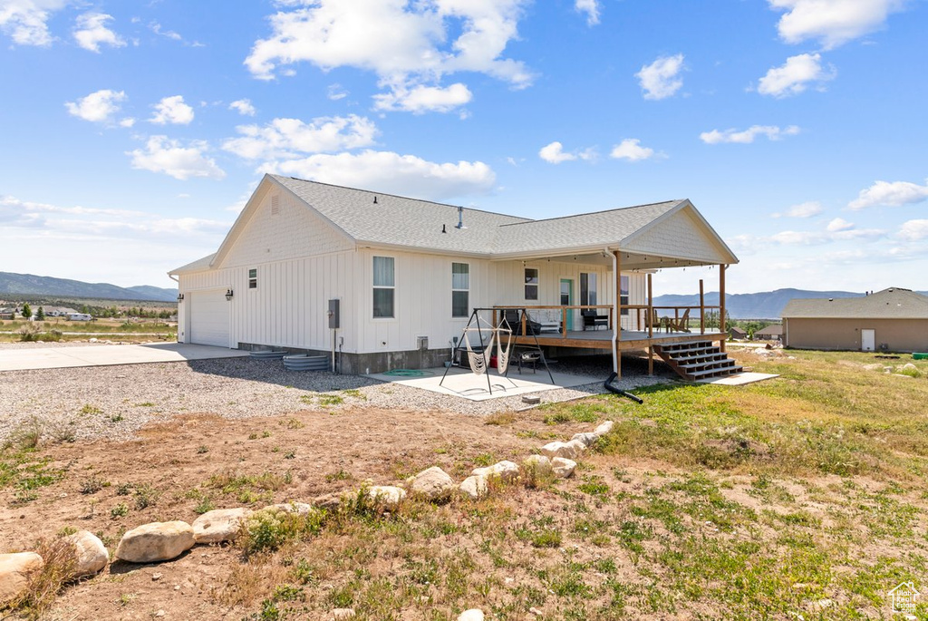 Rear view of house featuring an attached garage, a deck with mountain view, board and batten siding, concrete driveway, and a patio area